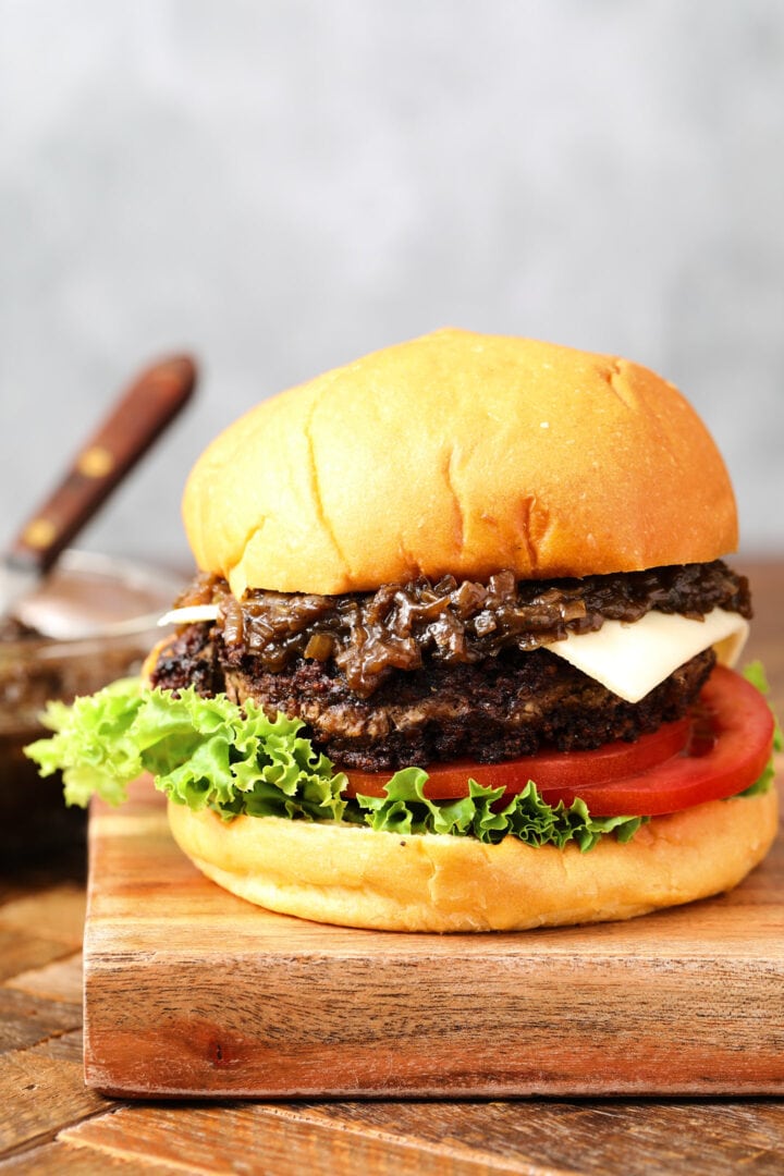 cheeseburger with caramelized onions and a slice of white cheese. There is a slice of lettuce and a few slices of tomatoes on the bottom of the burger.