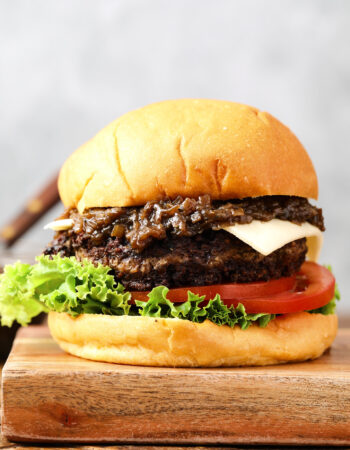 cheeseburger with caramelized onions and a slice of white cheese. There is a slice of lettuce and a few slices of tomatoes on the bottom of the burger.