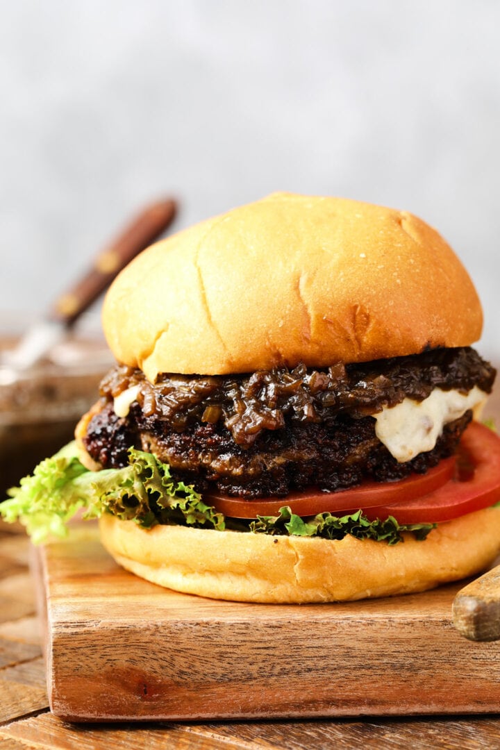 cheeseburger with caramelized onions and a slice of white cheese. There is a slice of lettuce and a few slices of tomatoes on the bottom of the burger.