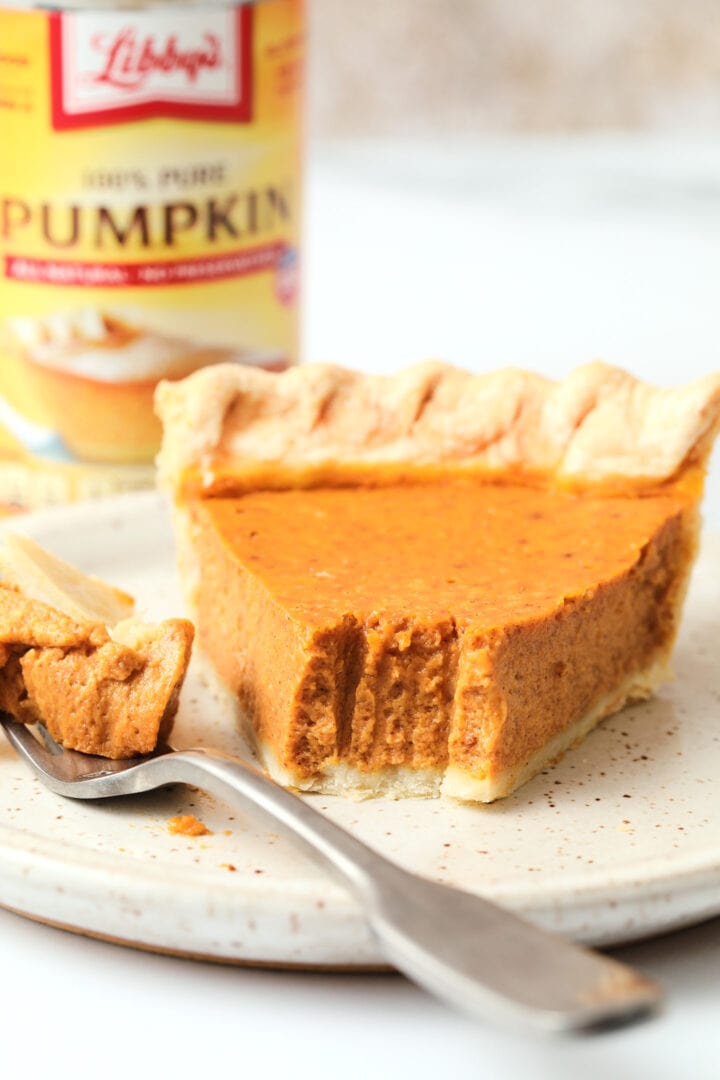 slice of pumpkin pie on a white speckled plate, there is a small can of pumpkin puree in the background.