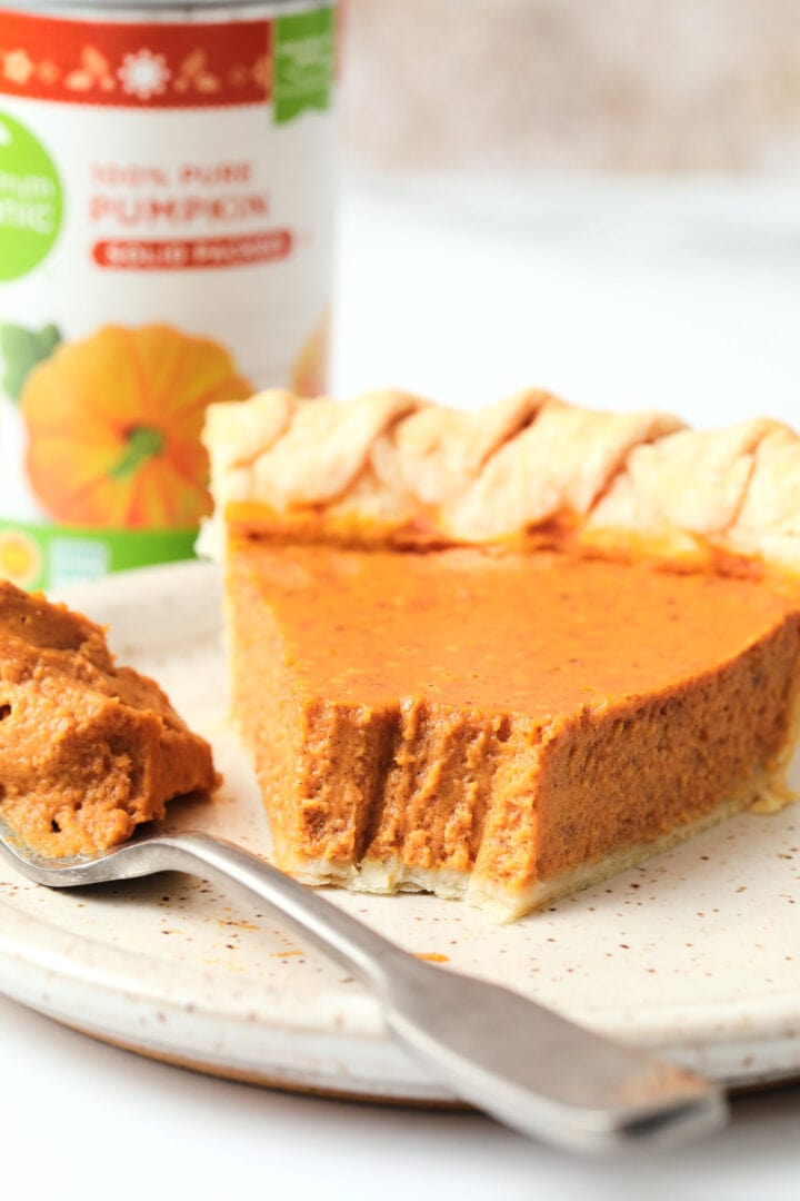 slice of pumpkin pie on a white speckled plate, there is a small can of organic pumpkin puree in the background.