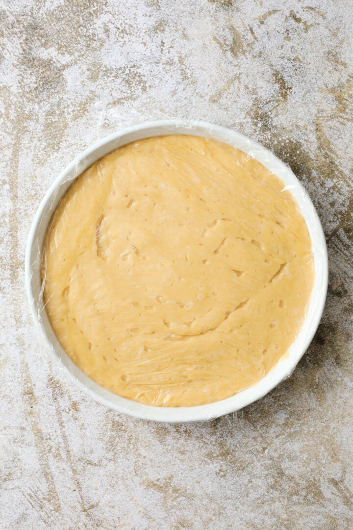 shallow dish of finished coconut custard. There is a layer of plastic over top of the surface of the custard.