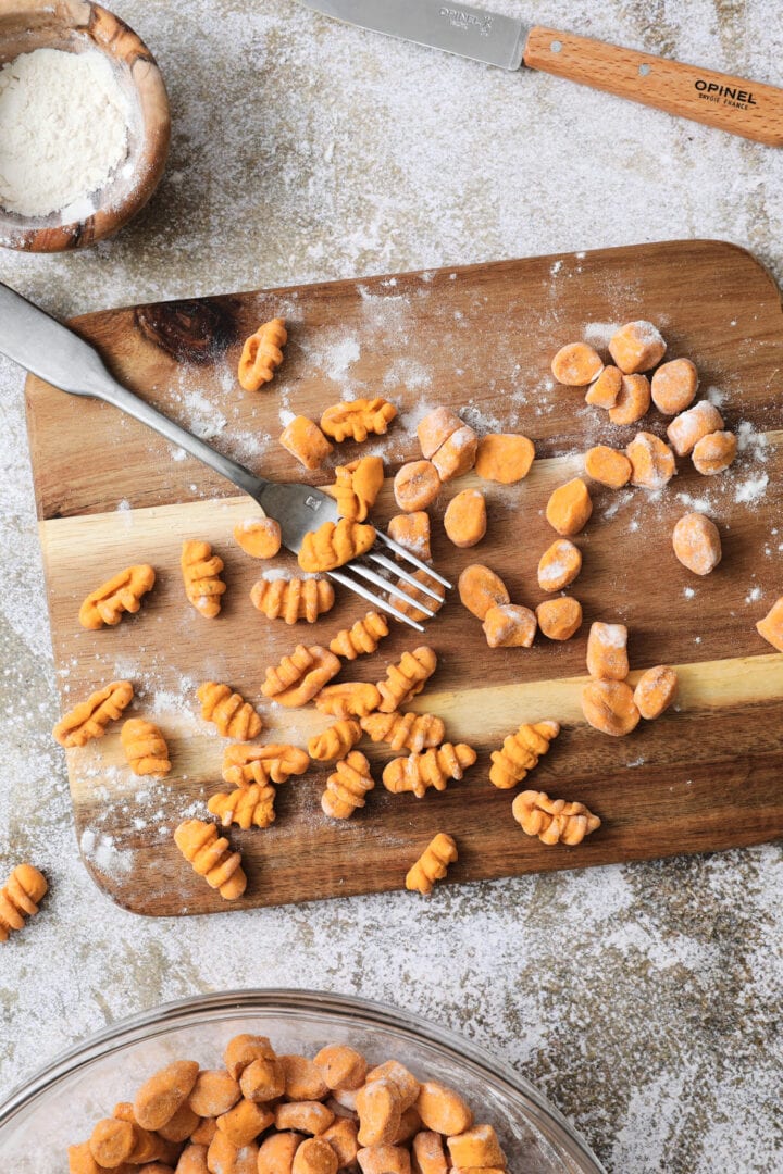 Small wooden cutting board that is dusted with flour and has shaped gnocchi pieces on it.