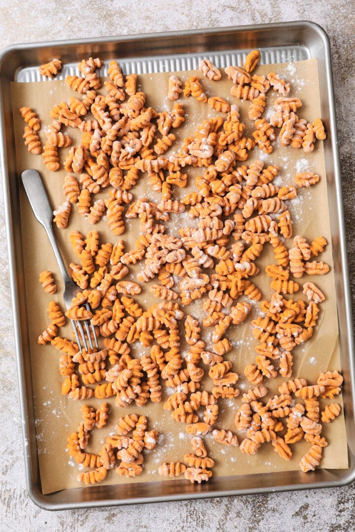 silver sheet pan of orange pumpkin gnocchi before being boiled. There is a sprinkle of flour and a fork on the side of the pan.