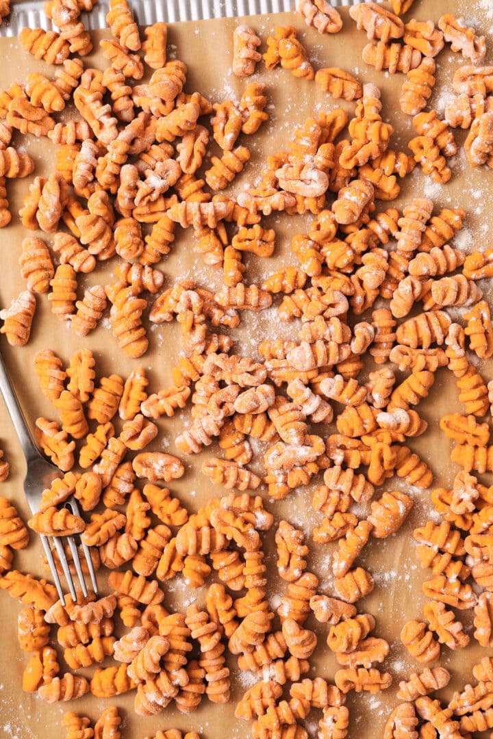 silver sheet pan of orange pumpkin gnocchi before being boiled. There is a sprinkle of flour and a fork on the side of the pan.