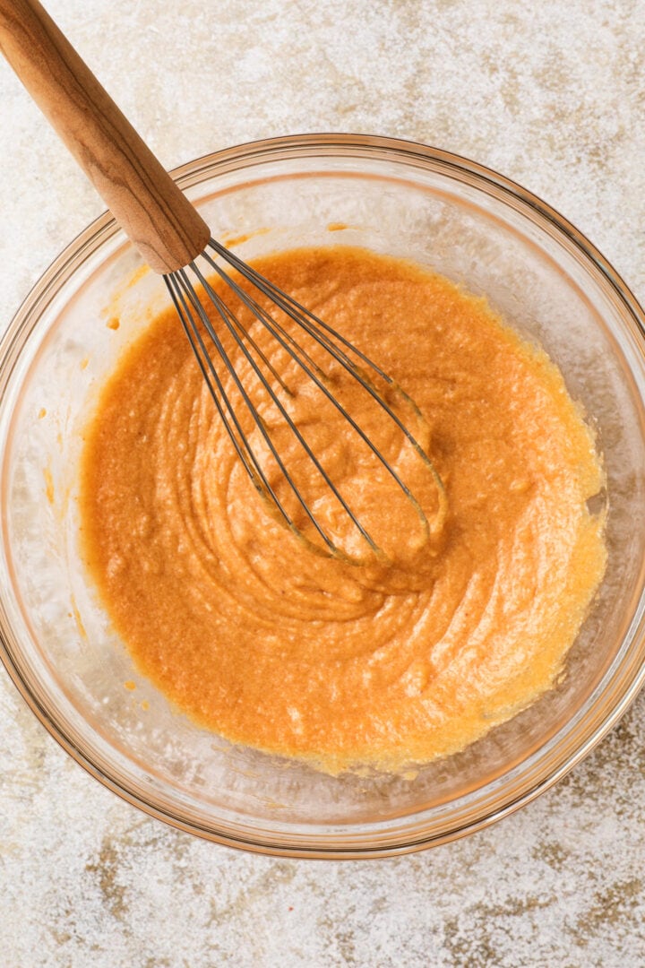 pumpkin loaf batter being folded together in a large glass mixing bowl.