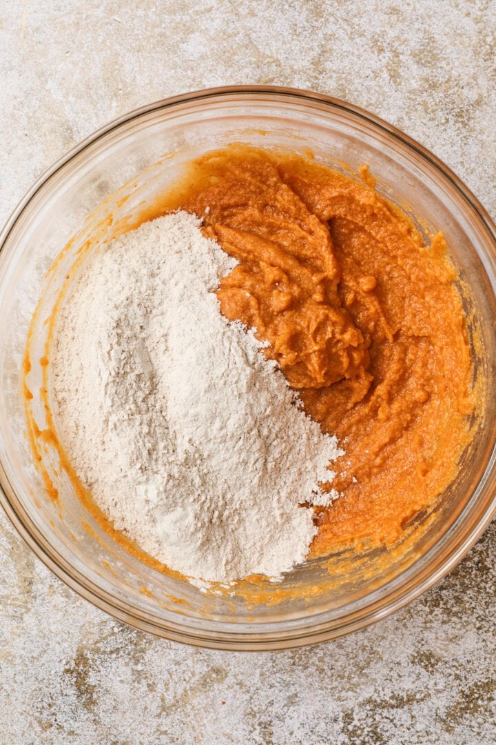 pumpkin loaf batter being folded together in a large glass mixing bowl.