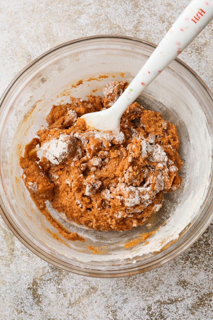 pumpkin loaf batter being folded together in a large glass mixing bowl.