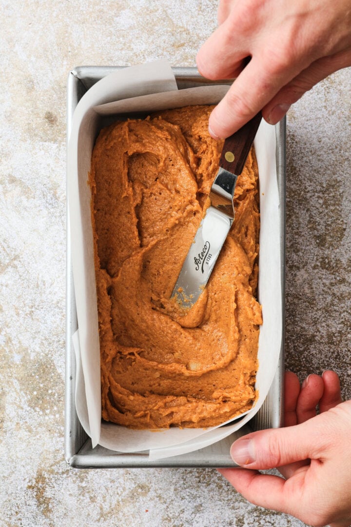 pumpkin loaf batter being spread into a prepared loaf pan.