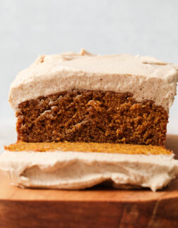 sliced pumpkin loaf resting on a wooden serving platter. There is a thick layer of frosting on the loaf.