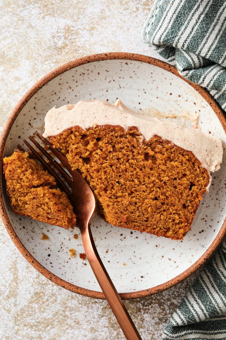 small white speckled plate with a slice of pumpkin loaf. There is a rose gold fork cutting into the slice.