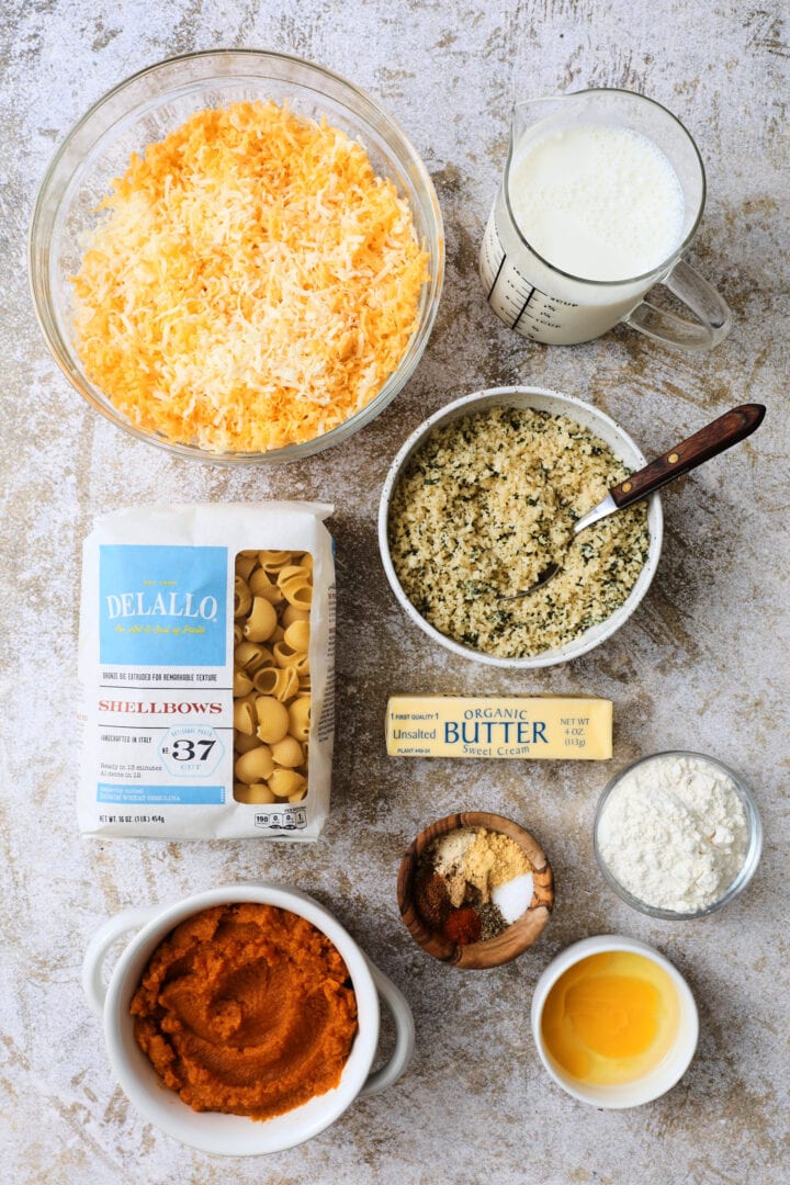 ingredients to make pumpkin macaroni and cheese, including pasta, butter, egg, flour, spices, pumpkin puree, seasoned breadcrumbs, cheese and milk.