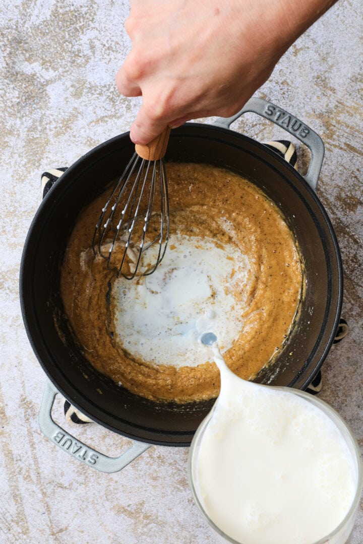 Cream being poured into the pot of seasoned flour to create a roux to thicken the sauce.