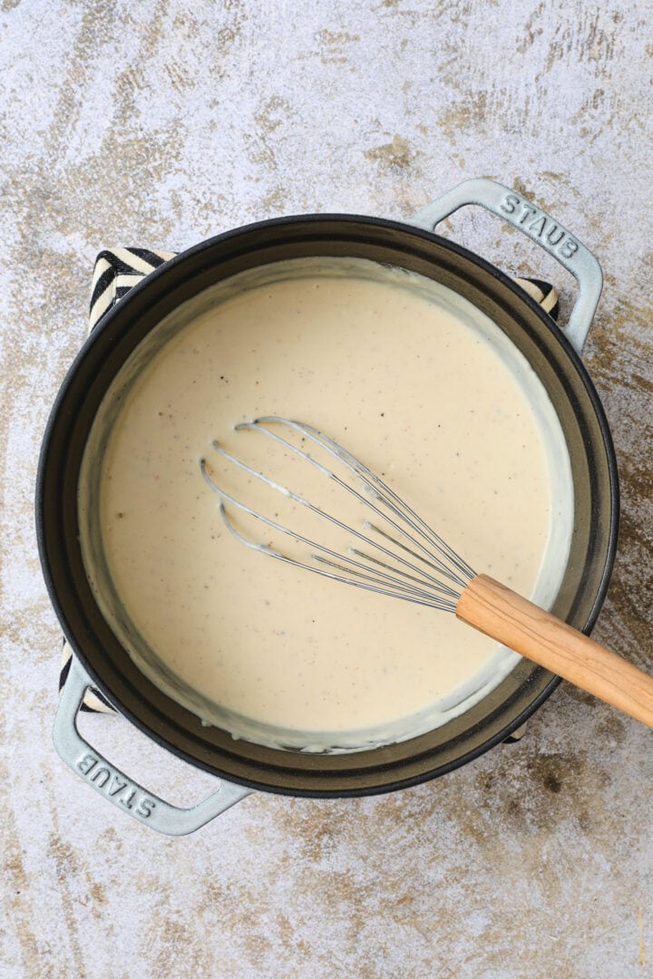 creamy sauce before the cheese has been added. There is a whisk resting on the side of the pot.