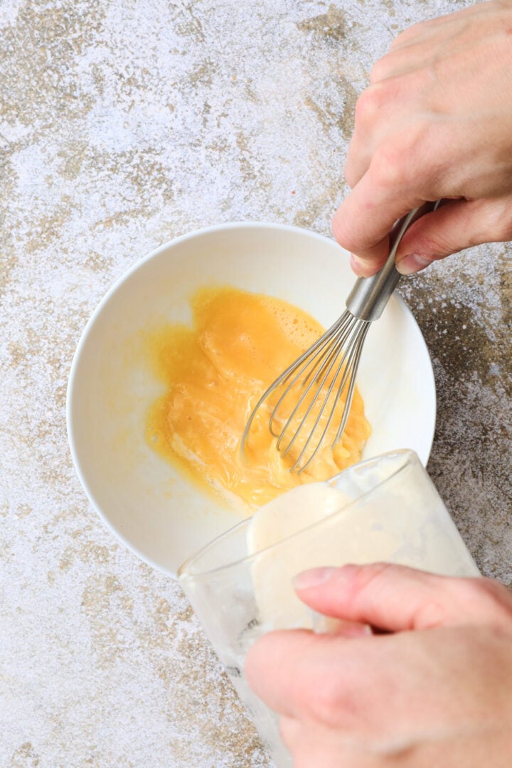 an egg being tempered by hot sauce in a small white bowl.