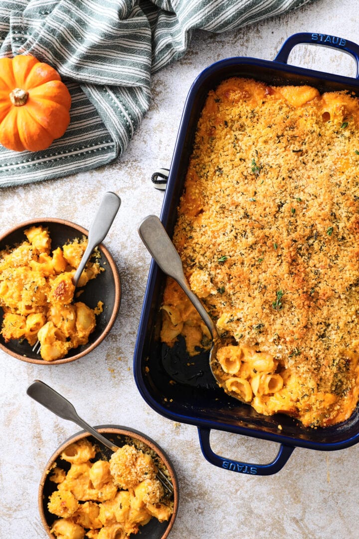 blue pan of pumpkin macaroni and cheese, with two dark plates off to the side.