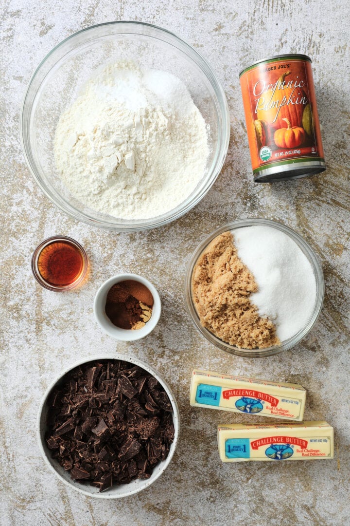 ingredients to make pumpkin chocolate chip skillet cookie, including pumpkin puree, flour, sugar, chopped chocolate, butter, vanilla and spices.