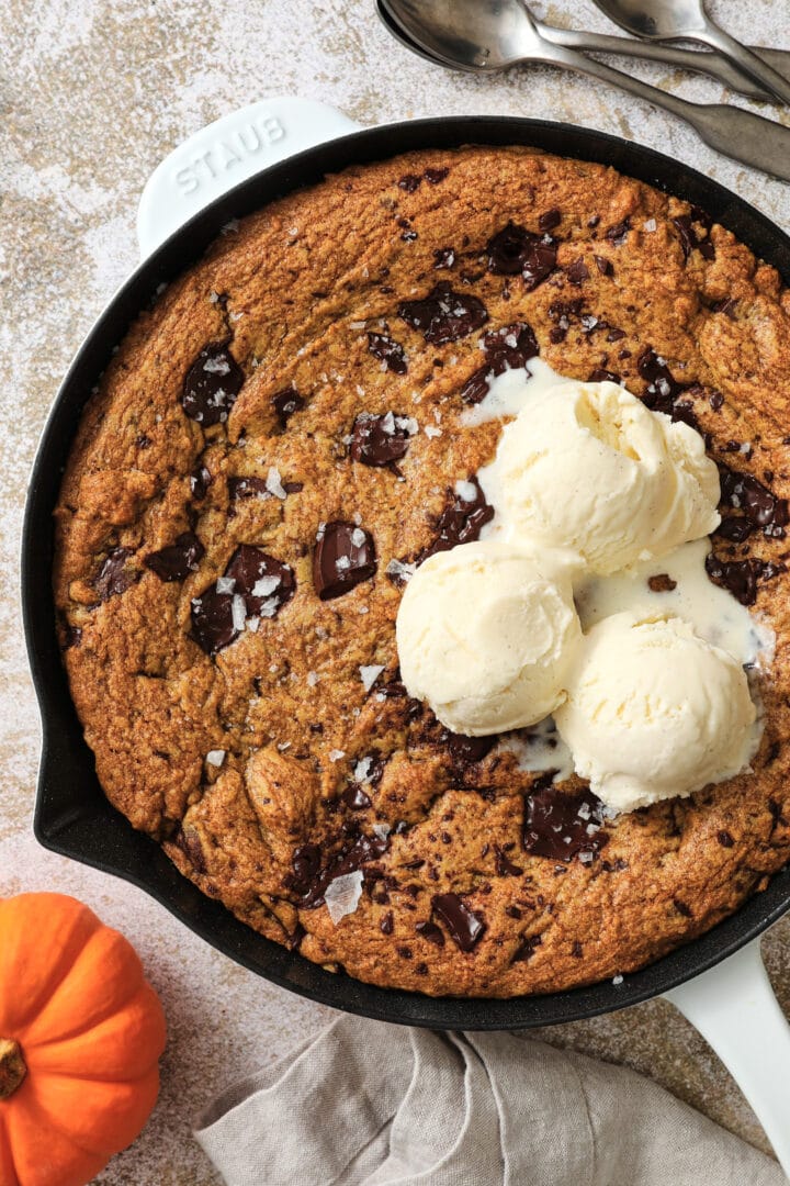 large pumpkin chocolate chip cookie with three scoops of vanilla ice cream on top.