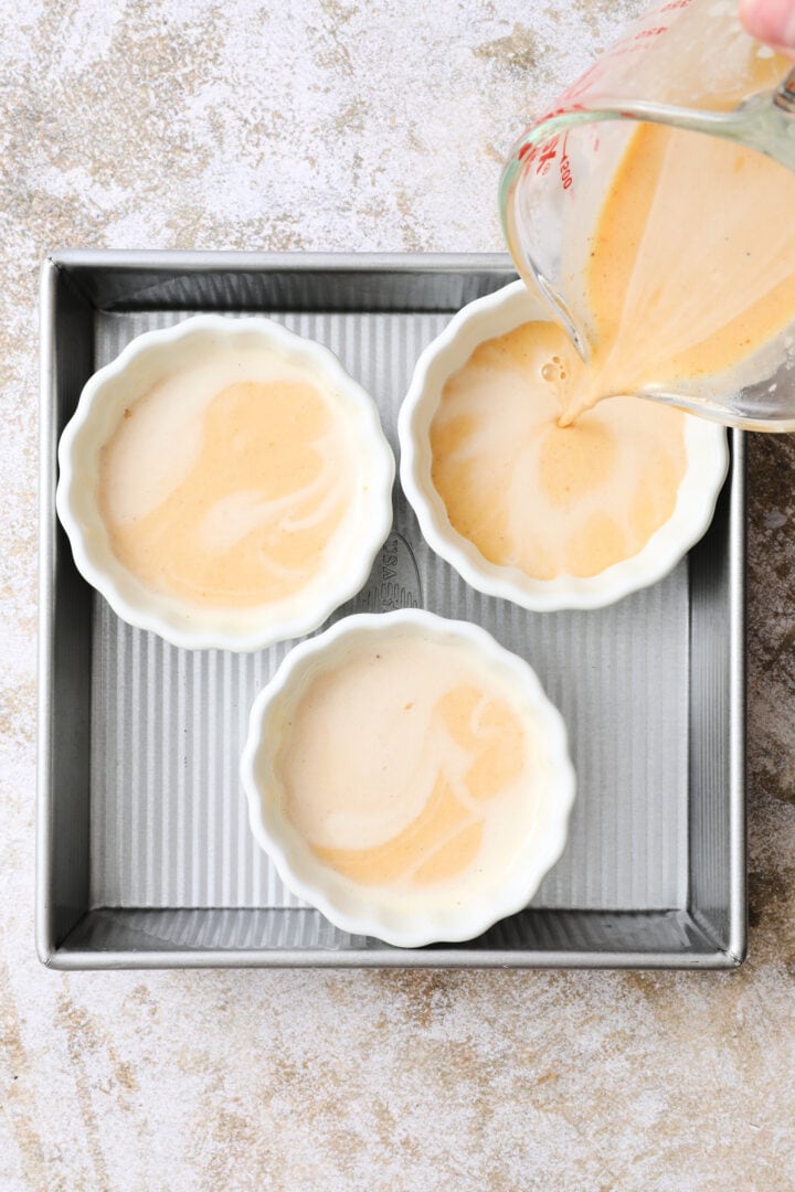 three white ramekins of pumpkin custard in a square metal pan.