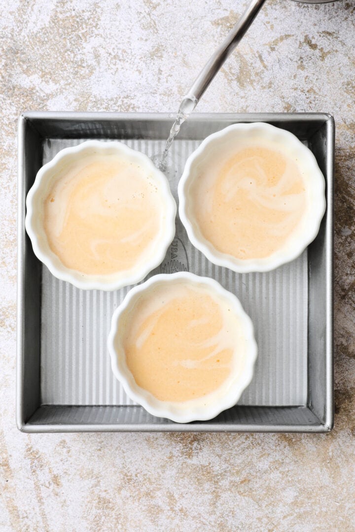 three white ramekins of pumpkin custard in a boiling water bath.