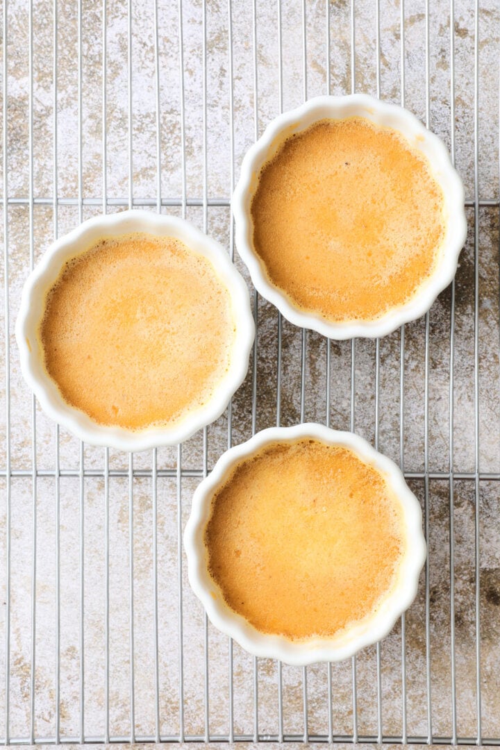 three white ramekins of just baked creme brulee custard. They do not have a sugar topping yet.