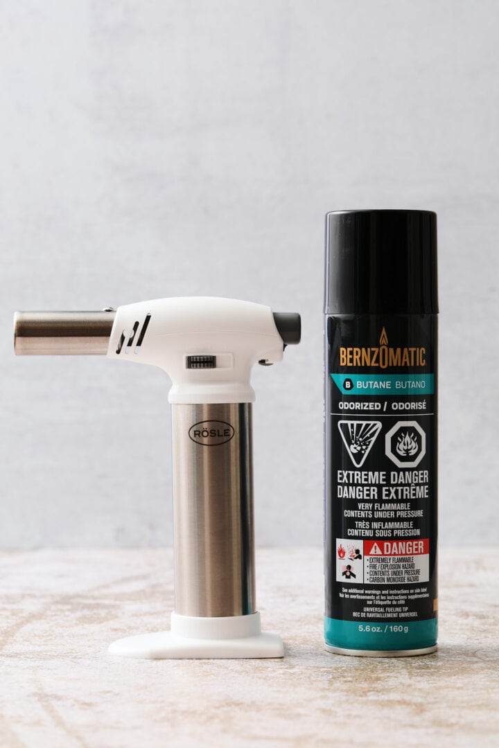 photo of a white kitchen torch and a can of butane for refilling.