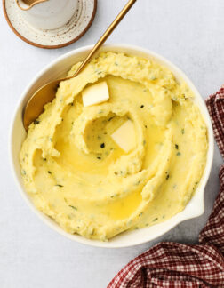 white bowl of creamy golden mashed potatoes with a golden spoon off to the side.