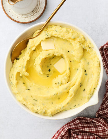 white bowl of creamy golden mashed potatoes with a golden spoon off to the side.