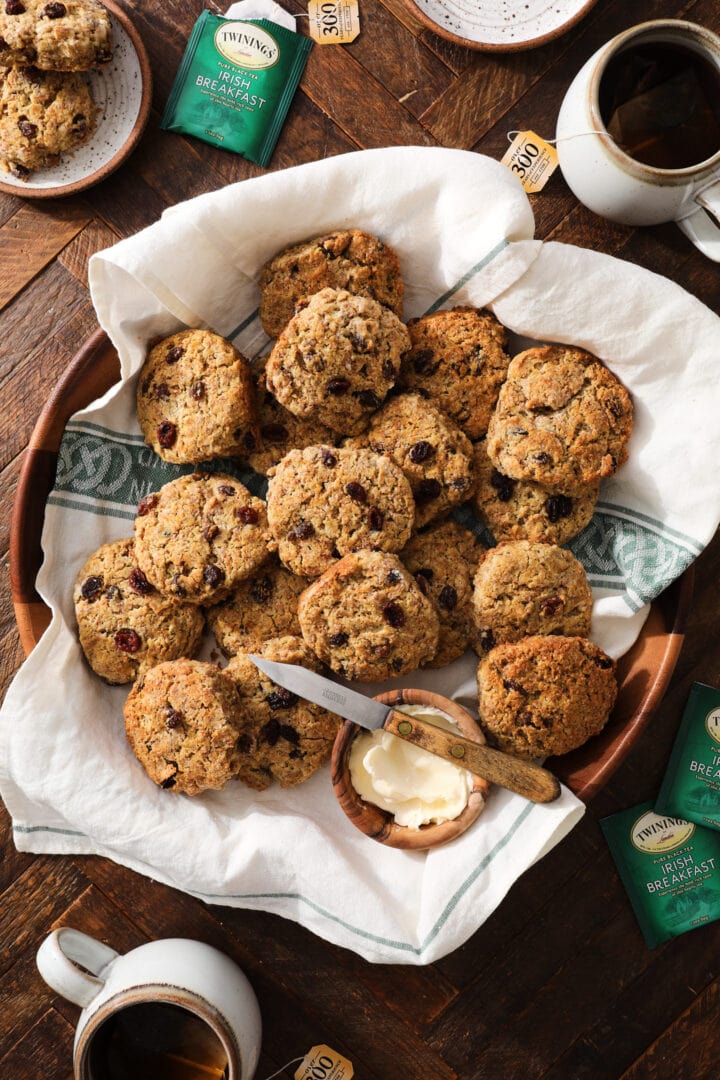 large wooden platter filled with brown bread biscuits with raisins. There is a white towel beneath the biscuits.