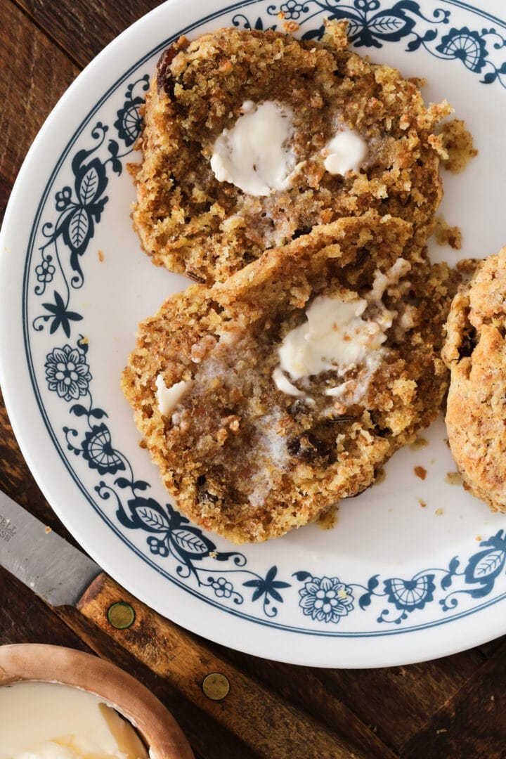 brown raisin biscuit cut in half and spread with butter on a small blue and white plate.